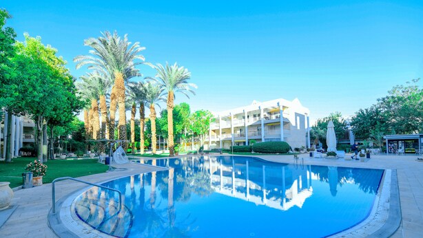 A swimming pool surrounded by palm trees and a building with balconies.