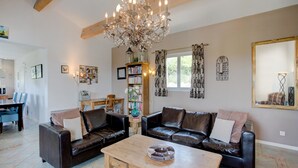 A living room with a chandelier, leather sofas, a wooden coffee table, and a bookshelf. - Stylish Family Villa in Félines (Félines-Minervois)