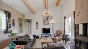 A living room with a sofa, a coffee table, a television, a fireplace, and a chandelier. - Stylish Family Villa in Félines (Félines-Minervois)