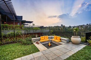 Un área de estar exterior moderna con un brasero, rodeada de vegetación y vistas al paisaje.