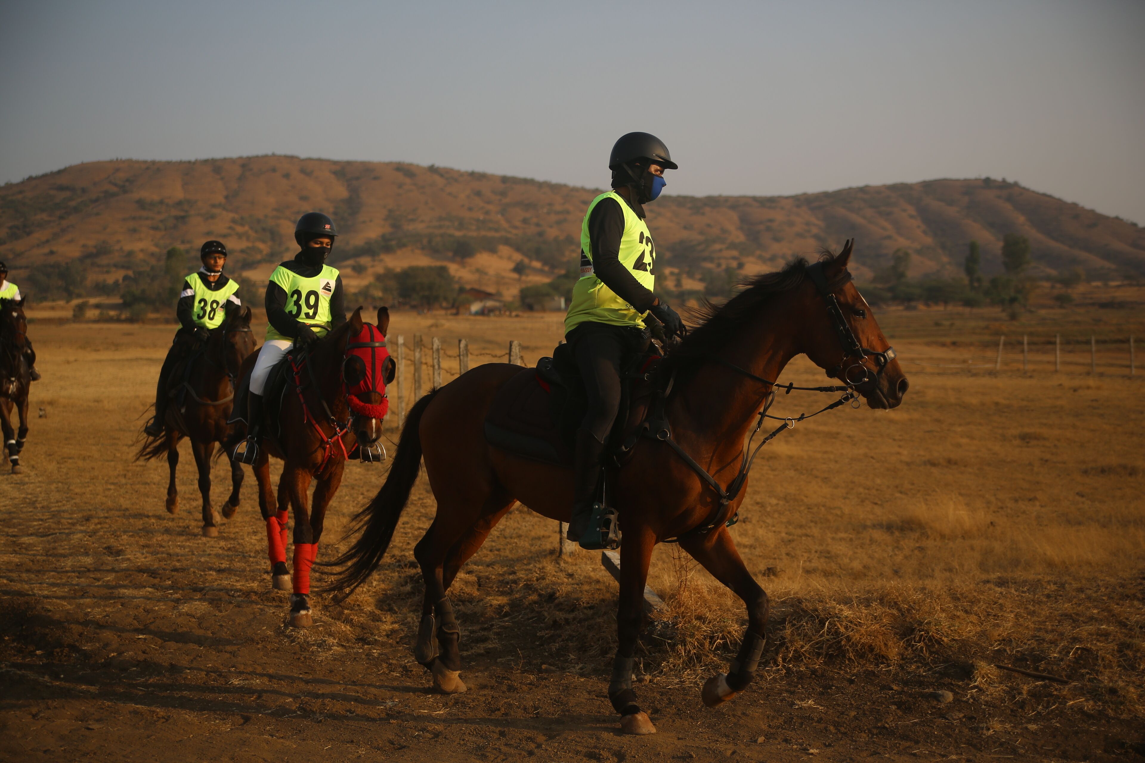Un grupo de jinetes a caballo en un campo seco y abierto, con colinas al fondo.