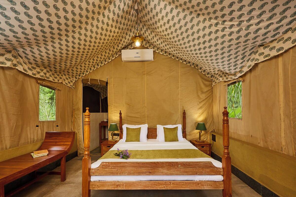 A tent-style room with a wooden four-poster bed, two nightstands, a bench, and a red rug.
