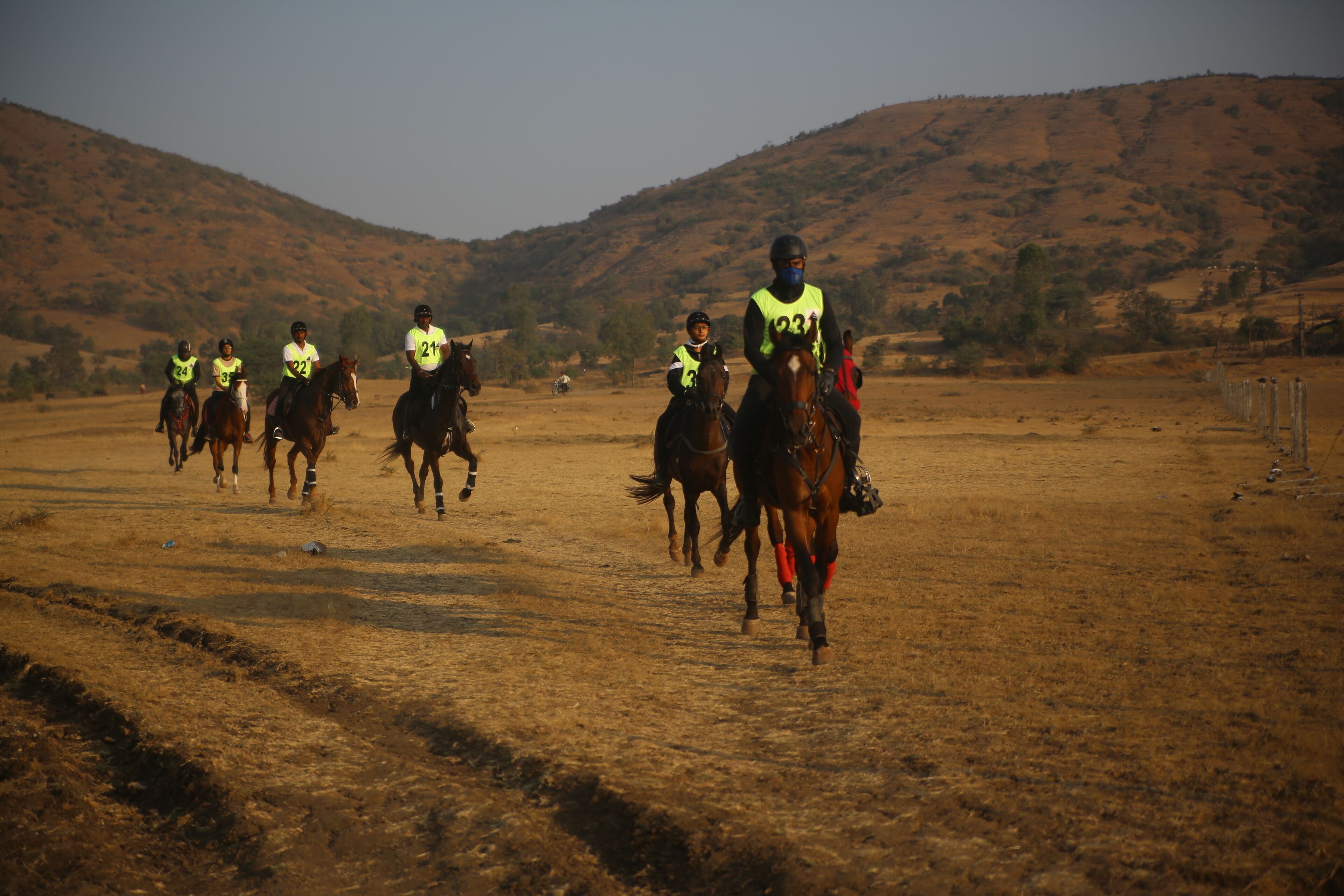 Un grupo de jinetes a caballo en un campo seco y abierto, con colinas al fondo.