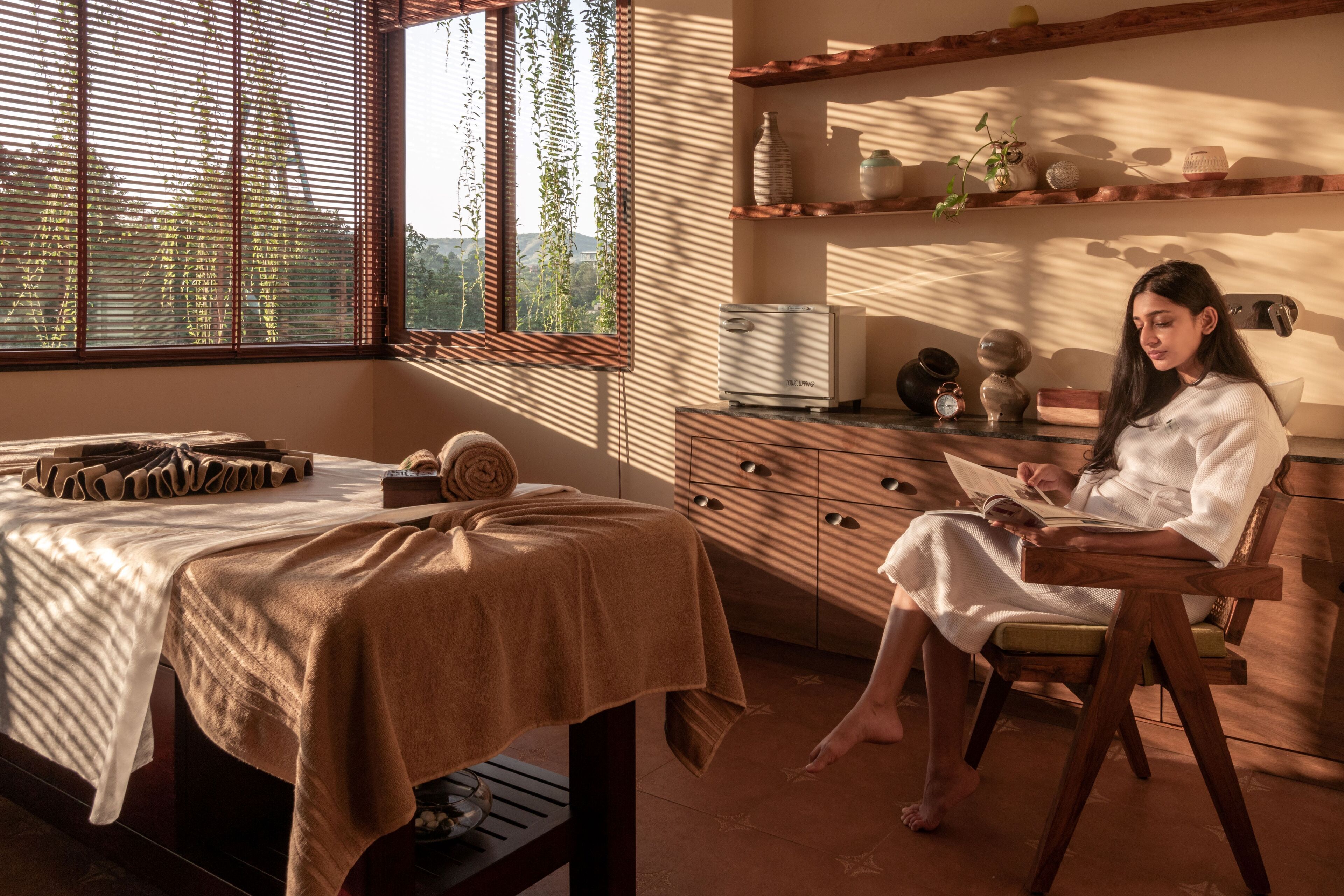 A room with a massage table, a chair, and a person reading a book.