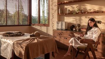 A room with a massage table, a chair, and a person reading a book.