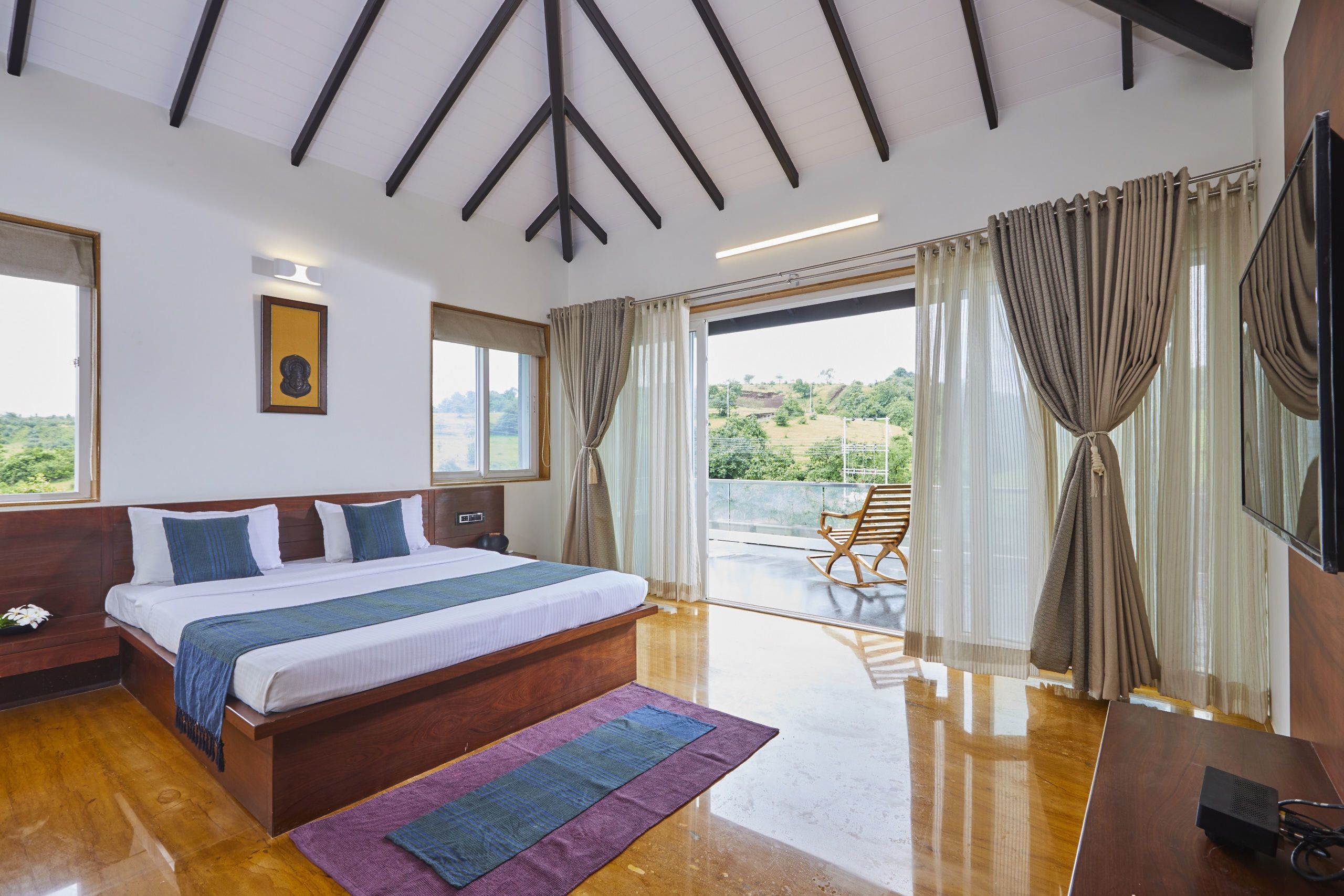 Un dormitorio espacioso con una cama grande, cabecero de madera y vistas al exterior a través de una puerta corrediza de vidrio.