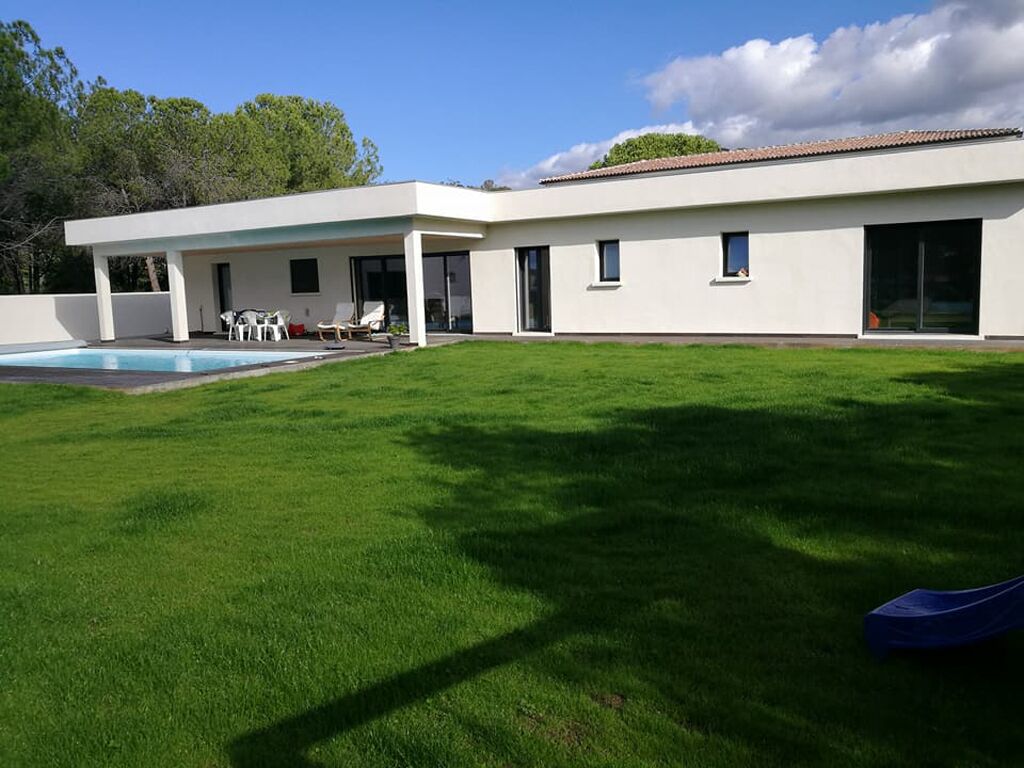 A modern house with a swimming pool, a covered patio, and a well-maintained lawn.