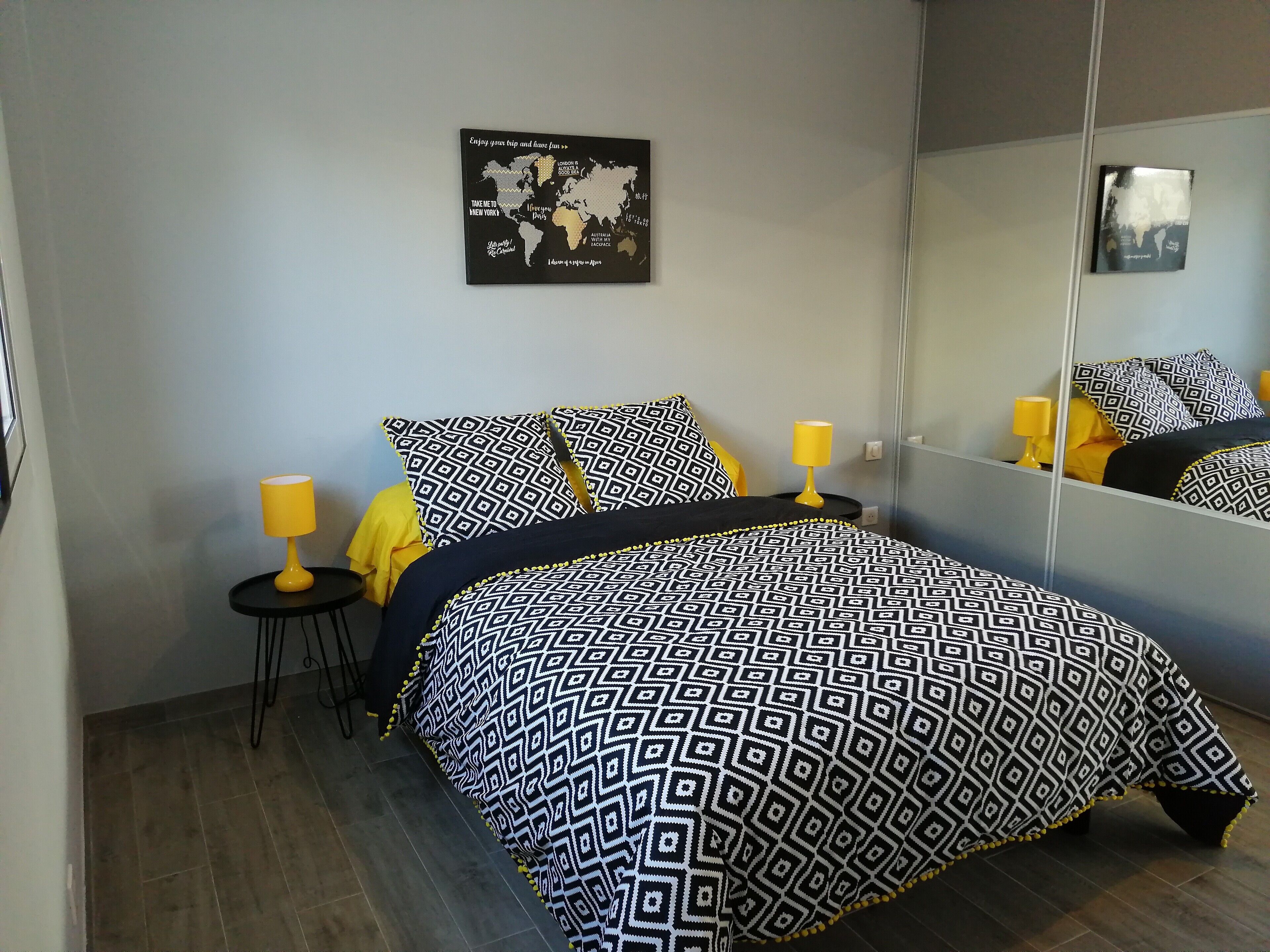 A bed with a patterned bedspread, a small bedside table with a lamp, and a wall-mounted map.