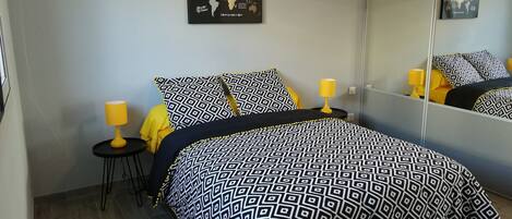 A bed with a patterned bedspread, a small bedside table with a lamp, and a wall-mounted map.