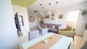 Una sala de estar moderna con un sofá, una mesa de comedor y sillas. Hay un televisor montado en la pared, un reloj y varios objetos decorativos.