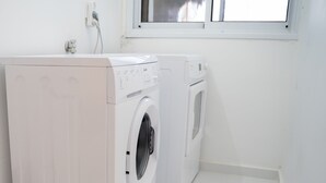 Un lavadero con dos lavadoras blancas y una ventana encima.