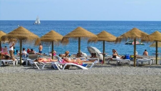 Una playa con sombrillas de paja y tumbonas.