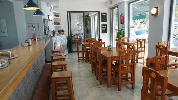 A café with wooden tables and chairs, a marble floor, and a counter with a blue pendant light. - Hostal Puerto Beach (Motril)