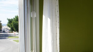 Una habitación con una pared verde, una ventana con cortinas blancas, una mesita de noche de madera y una cama con ropa de cama a rayas.
