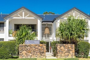 Stunning two-story residence with a grand entrance, flanked by lush greenery and surrounded by manicured hedges.