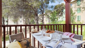 A table set for breakfast with plates, glasses, and pastries on a balcony with a view of trees and buildings. - Apartment in Cavalaire-sur-Mer near Beach (Cavalaire sur Mer)
