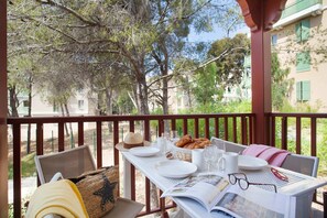 A table set for breakfast with plates, glasses, and pastries on a balcony with a view of trees and buildings. - Apartment in Cavalaire-sur-Mer near Beach (Cavalaire sur Mer)