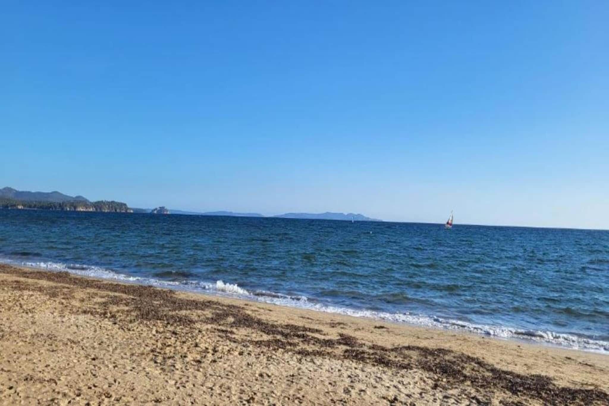 A beach with a clear sky, calm sea, and distant landforms.