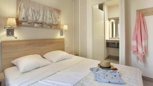 A hotel room with a bed, two wall-mounted lamps, a painting, a mirror, and a pink towel. - Apartment in Cavalaire-sur-Mer near Beach (Cavalaire sur Mer)