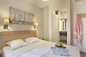 A hotel room with a bed, two wall-mounted lamps, a painting, a mirror, and a pink towel. - Apartment in Cavalaire-sur-Mer near Beach (Cavalaire sur Mer)