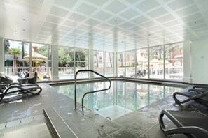 Una piscina interior con paredes de vidrio transparente, suelo de baldosas y techo con diseño geom étrico.