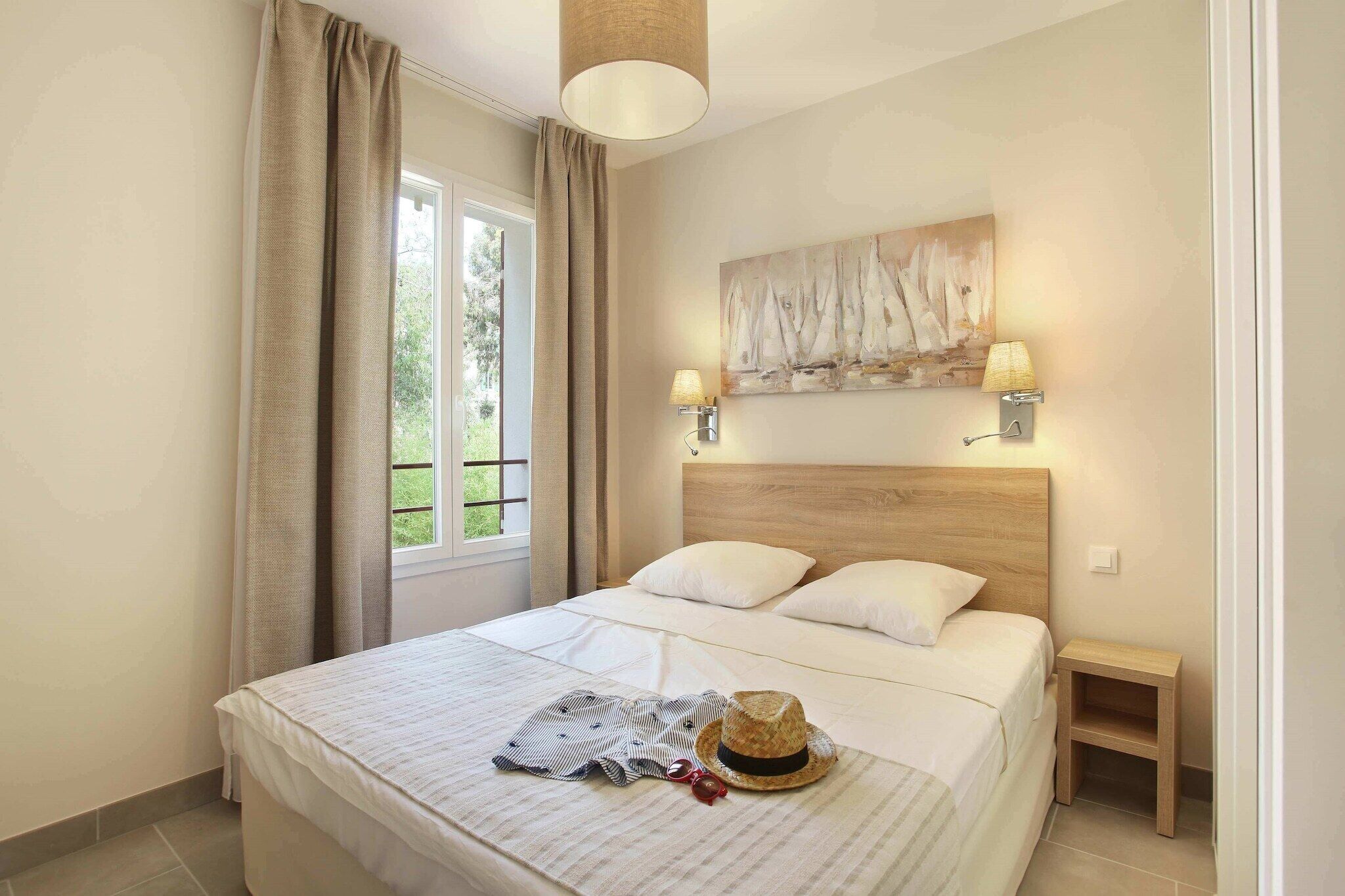 A hotel room with a bed, two bedside lamps, a painting, and a small bedside table.