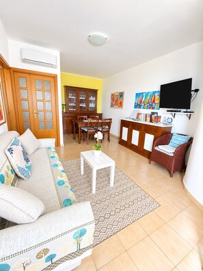 A living room with a sofa, dining table, chairs, a TV, and a cabinet.