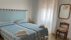 A bedroom with two beds, a chair, a nightstand, and a mirror. - Apartment/ flat -Cala Gonone  - Casa dolce vista - Via delle Ginestre 20 (Cala Gonone)