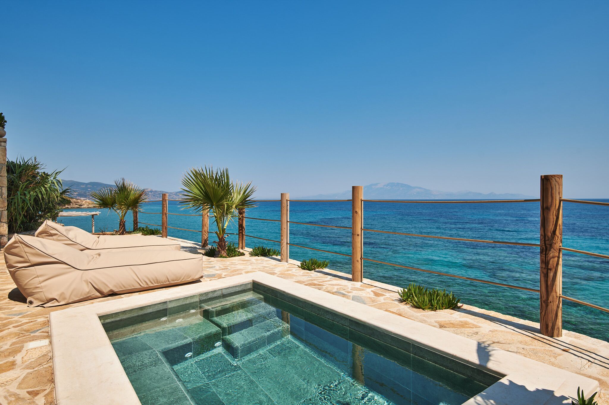 A pool area with a clear view of the sea, a wooden deck, and a lounge chair.