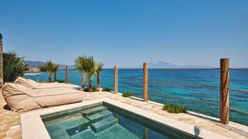 A pool area with a clear view of the sea, a wooden deck, and a lounge chair.