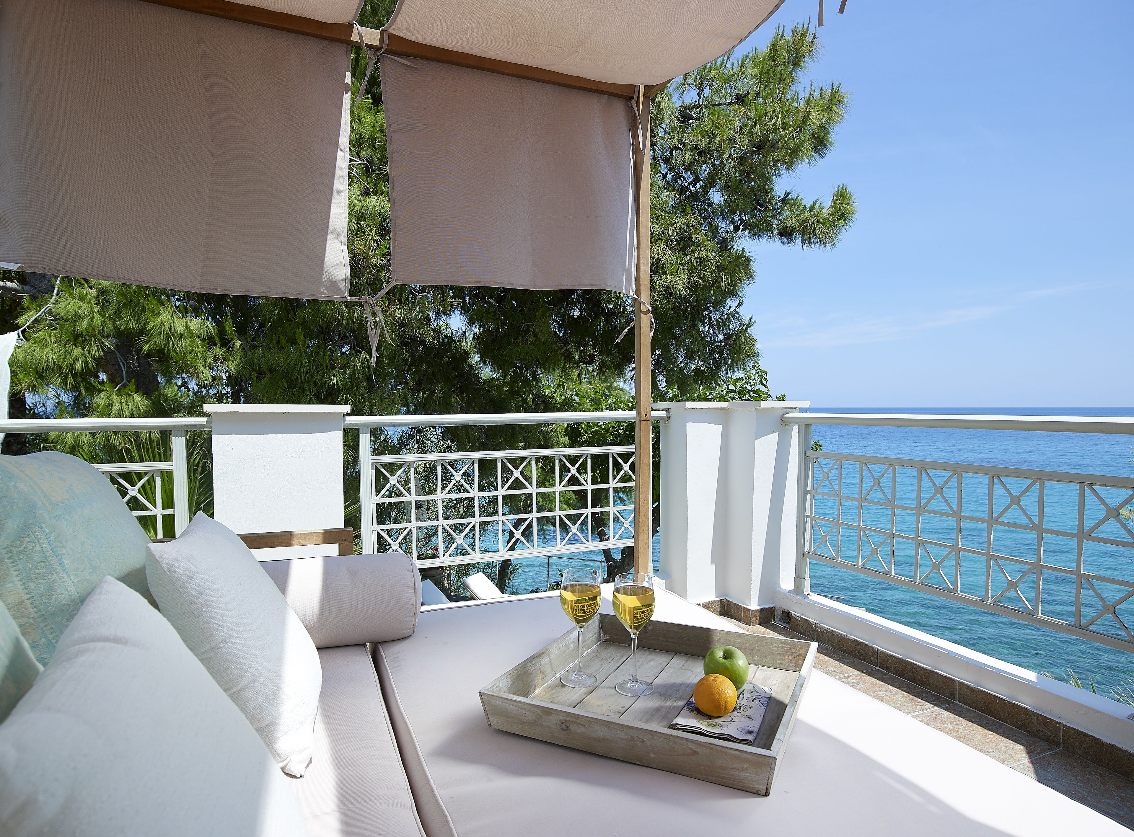 A balcony with a white cushioned seating area, a tray with a glass of wine, an apple, and an orange.