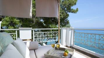 A balcony with a white cushioned seating area, a tray with a glass of wine, an apple, and an orange.