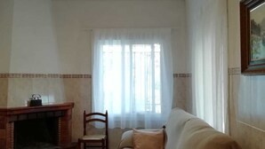 A living room with a fireplace, a sofa, a chair, and a window with sheer curtains. - Beautiful country house with private pool in Elche for 7 people. (elche)
