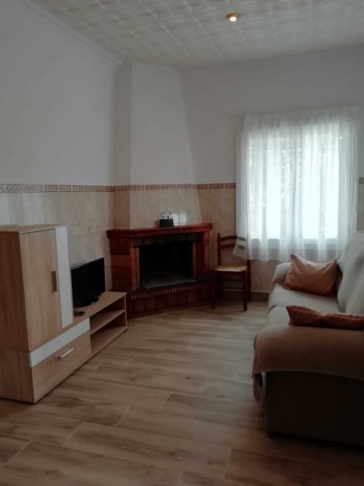A living room with a fireplace, a television on a wooden cabinet, a sofa, and a window with sheer curtains.
