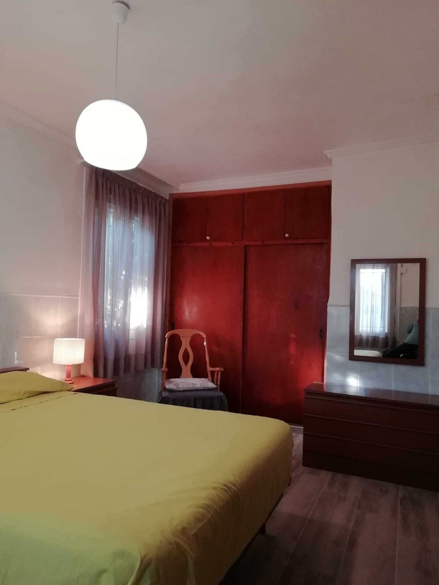 Une chambre d’hôtel avec un lit, une chaise, une commode, un miroir et une lampe.