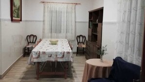 A dining area with a table set for four, a sofa, a small round table with a plant, and a bookshelf. - Beautiful country house with private pool in Elche for 7 people. (elche)