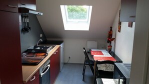 Une cuisine compacte équipée d’une cuisinière, d’un évier et d’une fenêtre. On y trouve une table à manger avec des chaises et un vase rempli de fleurs.