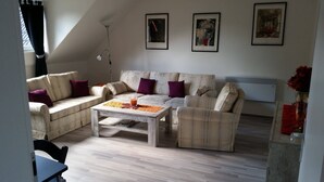 Un salon comprenant un canapé, une table basse et un lampadaire. Trois œuvres d’art encadrées ornent le mur.