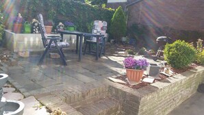 Un espace patio aménagé avec une table et des chaises, entouré de plantes en pot et d’un mur en briques.