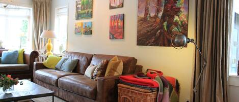 A living room with a brown leather sofa, a coffee table, and a large painting on the wall.