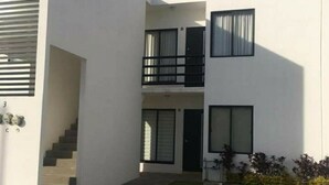 A modern two-story building with a flat roof, a staircase leading to the upper level, and a small front yard with grass and plants. - departamento duplex increible! (Fraccionamiento Las Ceibas)