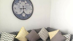 A modern living room with a grey sectional sofa, patterned throw pillows, a round wooden coffee table, and a decorative wall clock. - departamento duplex increible! (Fraccionamiento Las Ceibas)