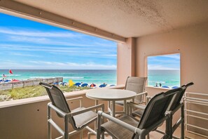 Un balcon avec vue sur la plage, une table ronde et deux chaises.