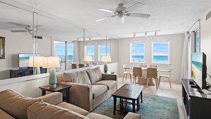 A hotel room with a sofa, a coffee table, a TV, a dining area with chairs, and a view of the beach through the windows. - Beach Front at Jetty East! One FREE Beach Chair Setup Each Day of Your Stay! (Destin)