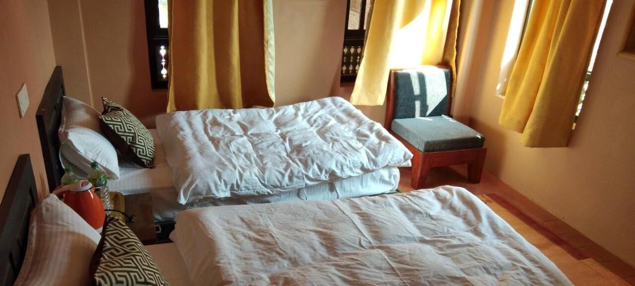 A hotel room with two beds, a small table, a chair, and a window with curtains.