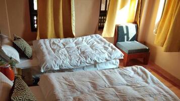 A hotel room with two beds, a small table, a chair, and a window with curtains.