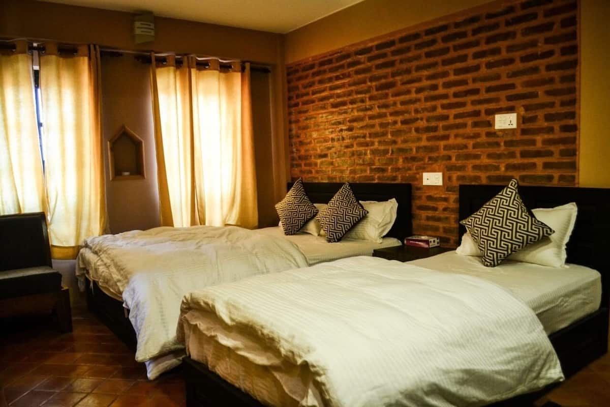 A hotel room with two beds, a brick wall, and a window with curtains.