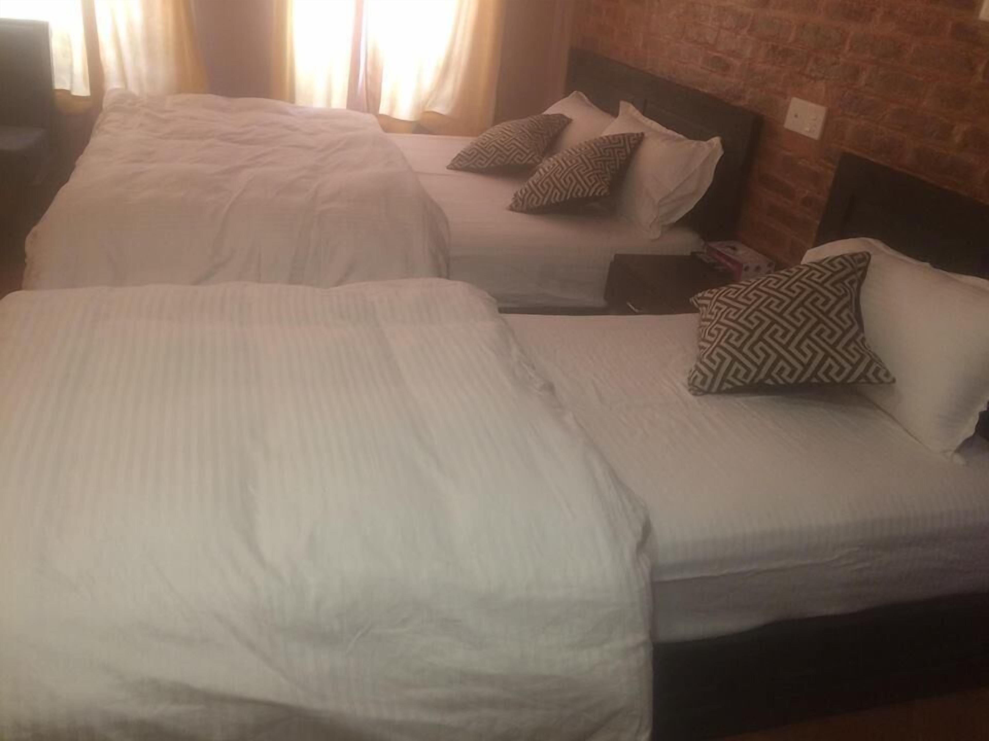 Twee eenpersoonsbedden met witte lakens en gestreepte kussens in een kamer met een bakstenen muur.