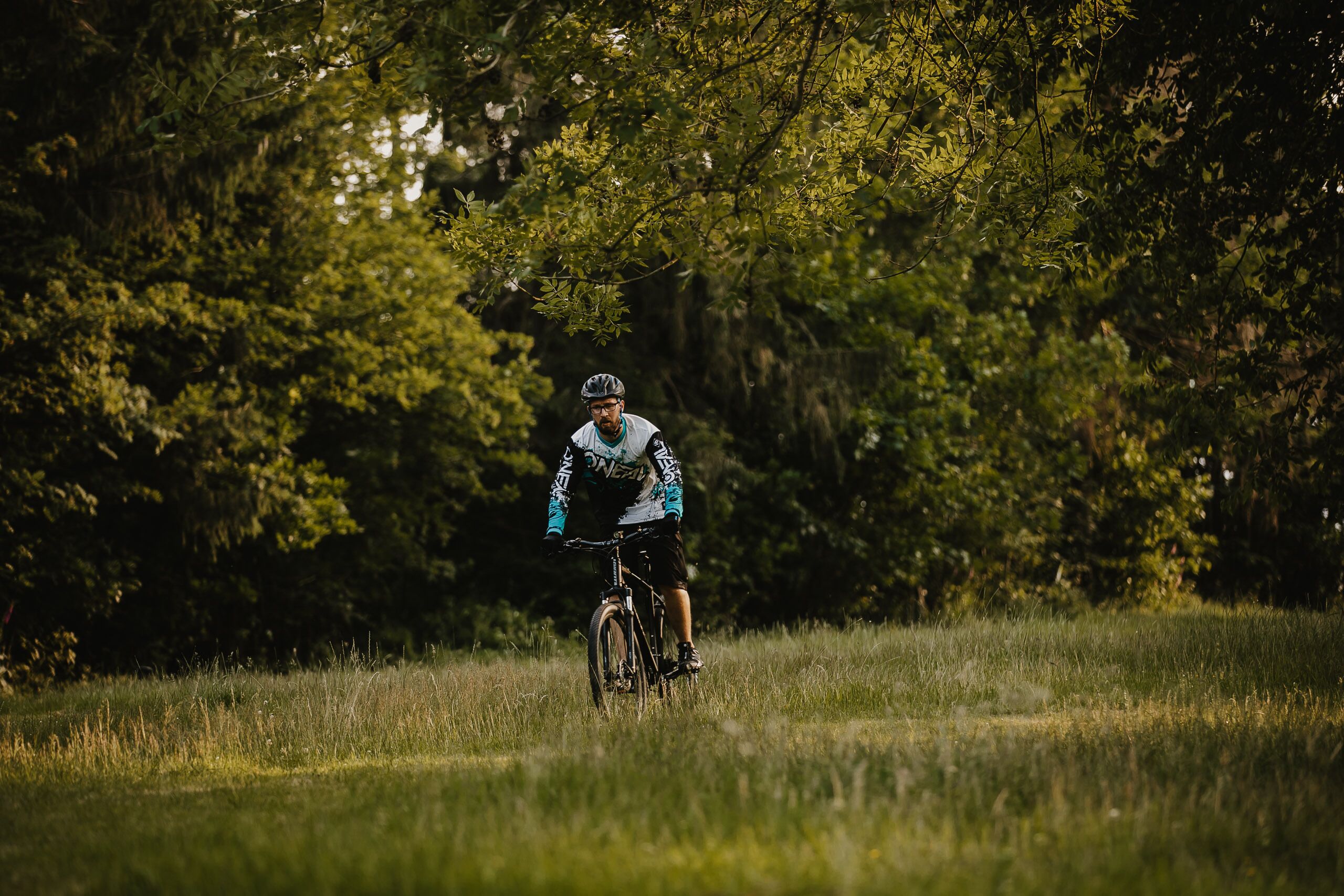 Una persona va en bicicleta per un camp amb arbres al fons.