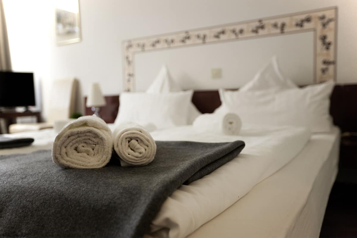 Un lit bien fait, avec des draps blancs et une serviette enroulée posée sur une couverture gris foncé.